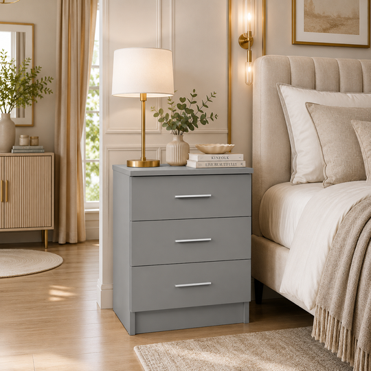 Grey 3 drawer bedside table with silver handles beside a modern bed